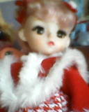 a bust shot of a pale doll with pale pink hair dressed in red